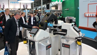 Auf dem Stand der Robert Bosch AG: Ein Messebesucher testet gerade die Funktionstüchtigkeit der Sensorhaut des Apas-Assistant von Bosch. Die projektiven Sensoren in der schwarzen Lederhülle um den Roboterarm detektieren die Annäherung und stoppen die