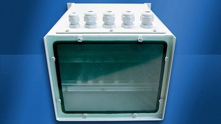 Vorderansicht des geschlossenen Heitec-Gehäuses mit fünf PG-Verschraubungen auf dem Deckblech und Makrolon-Platte als Frontabdeckung.