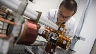 Der Wissenschaftler Wenqi Hu, der an der Studie mitgewirkt hat, bedient in einem Labor im Max-Planck-Institut für Intelligente Systeme einen Aufbau, in dem ein Miniroboter, der in einer Schale liegt, von Spulen umgeben ist.