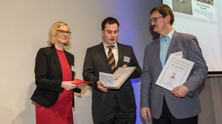 Stefanie Eckardt, leitende Redakteruin der Elektronik automotive, verleiht Lukas Franzky und Prof. Dr.-Ing. Homeyer Urkunde und Auszeichnung für ihren tiefgreifenden Fachartikel zum Thema »kHz-Rippelstrom im Lichtbild«.