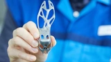 BMW Mitarbeiter hält ein Bauteil aus dem 3D-Drucker in der Hand