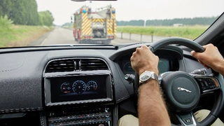 Fahrt hinter Rettungsfahrzeug mit Ansicht des Autodisplays mit Warnung vor Rettungsfahrzeug