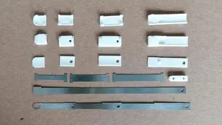Teile auseinandergebauter Finger. Sie bestehen aus drei übereinander gelegten Blattfedern, zusammengehalten durch Fingerglieder aus robustem und reibungsarmem Hochleistungskunststoff (weiß).