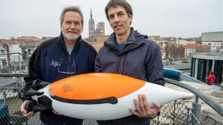 Rudolf Bannasch (l), Geschäftsführer der Firma EvoLogics, und Burkard Baschek, Ozeanograf und Direktor des Deutschen Meeresmuseums in Stralsund mit einem Prototypen einer Unterwasserdrohne in Pinguin-Form