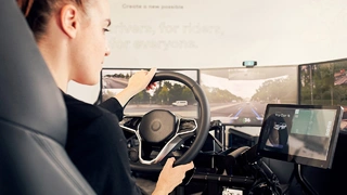 Die Vay-Telefahrer:innen sitzen an einer Telefahrstation mit Lenkrad und Pedalen. Von dort aus steuern sie das Auto bis zum gewünschten Ort.