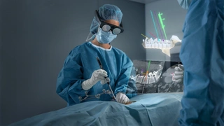 Chirurgen mit Brille und Instrumenten im OP, in der Luft schwebt die Projektion des Operationsfeldes als Anleitung, wie die Ärzte die Schrauben in die Wirbelsäule zu setzen haben.