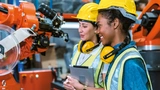 Zwei Mitarbeiterinnen mit Helm und Kopfhörer vor einem Lagerroboter